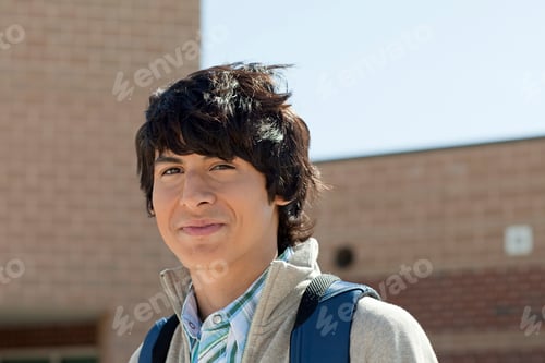 Preview: Smiling teenager with a backpack standing outside a school building