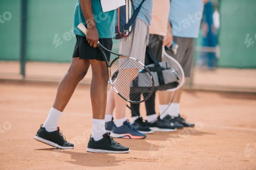Preview: partial view of multicultural sprotsmen with tennis equipment walking on court