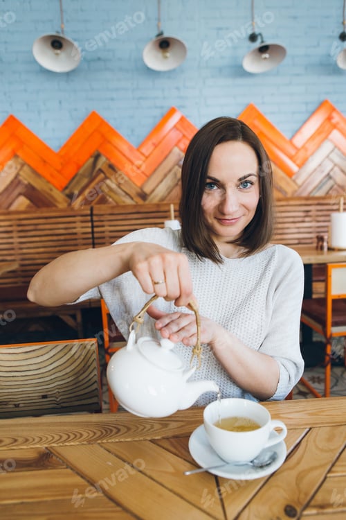 Preview: Young Pretty Brunette Woman Pours Green Tea From A Teapot Into A Cup In A Cafe. Toning.