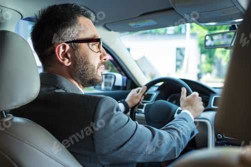 Preview: back view of businessman in suit and eyeglasses driving car alone