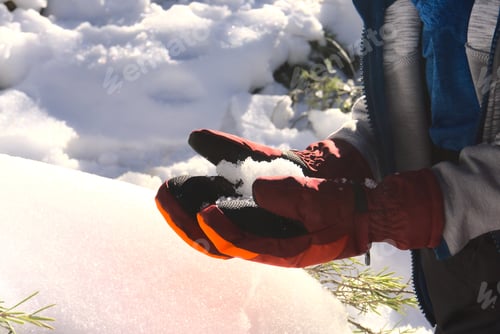 Preview: Boy's hands wearing gloves holding snow, snowy winter background