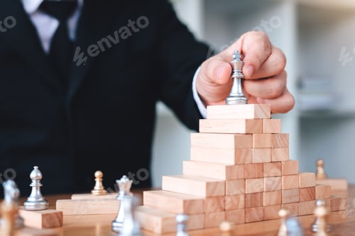 Preview: Businessman hand picking chess on top block wood about leadership concept.