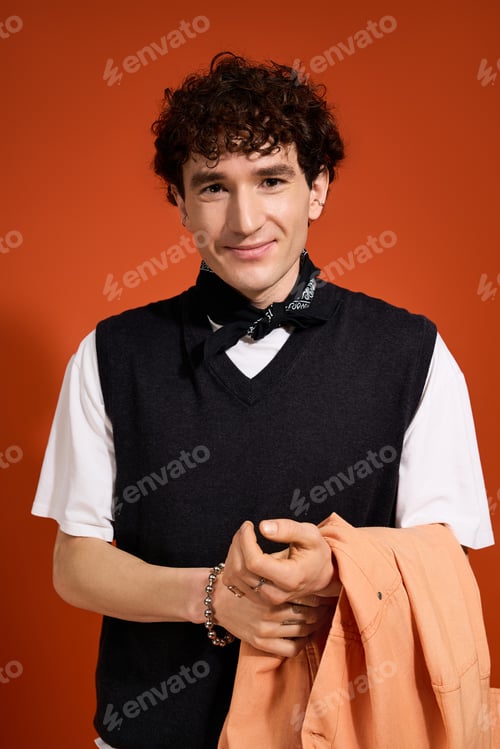 Preview: Stylish young man exudes charm with trendy outfit against vibrant orange backdrop