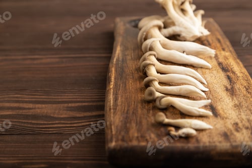 Preview: Raw Oyster mushroom, Pleurotus ostreatus on cutting board on brown wooden, Side view, copy space