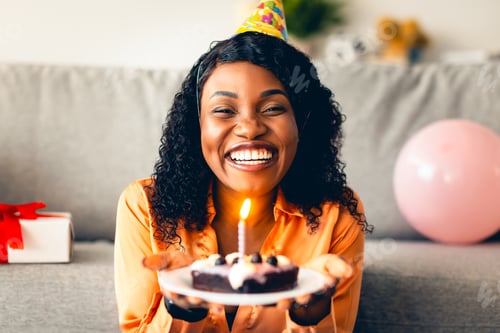 Preview: Cheerful Black Lady Holding Birthday Cake With Candle At Home