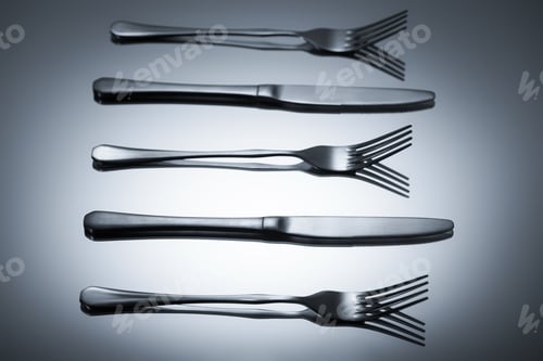 Preview: shiny stainless steel forks and knives reflected on grey