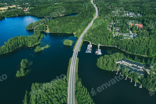 Preview: Aerial view of asphalt road with cars over blue lake and green woods in Finland