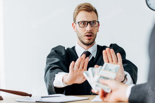 Preview: cropped view of man holding money near surprised judge in glasses gesturing in office