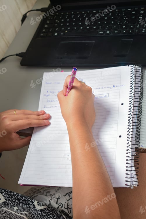 Preview: Selective focus shot of female writing some notes in a notebook from a laptop