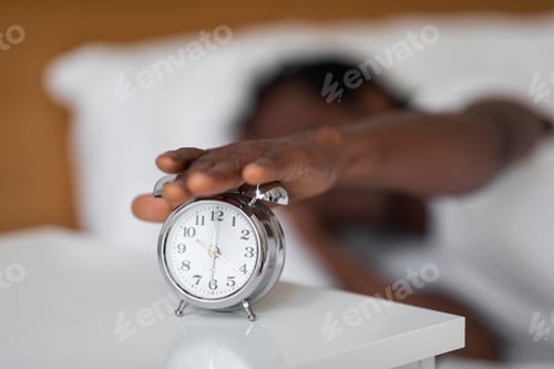 Preview: Unrecognizable Black Man Reaching Alarm Clock On Bedside Table With Hand