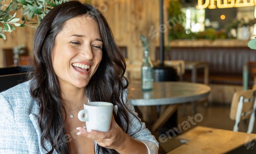 Preview: Joyful woman smiling while enjoying drinking a cup of coffee in a coffee shop.