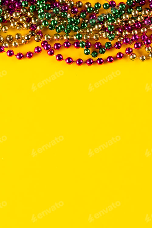 Preview: Composition of colourful mardi gras beads on yellow background with copy space