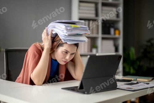 Preview: A woman is sitting at a desk with a laptop and a stack of papers on her head