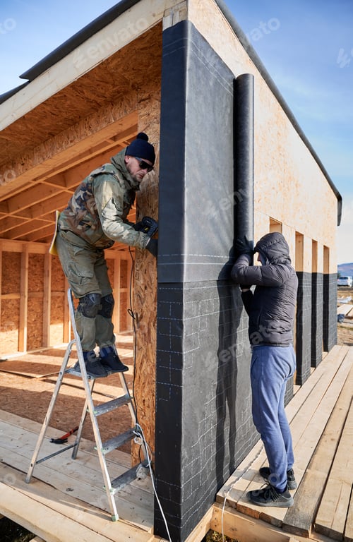 Preview: Male builder installing waterproof membrane on wall of future wooden frame house.
