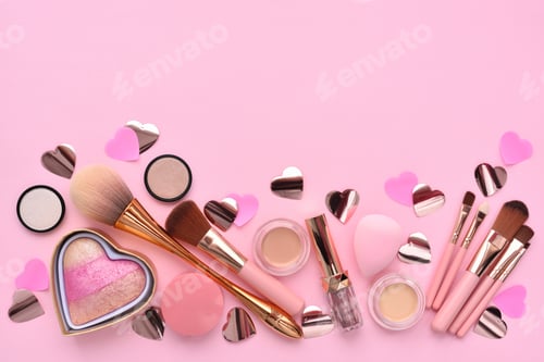Makeup brushes and decorative cosmetics, hearts on a pink background. Top view