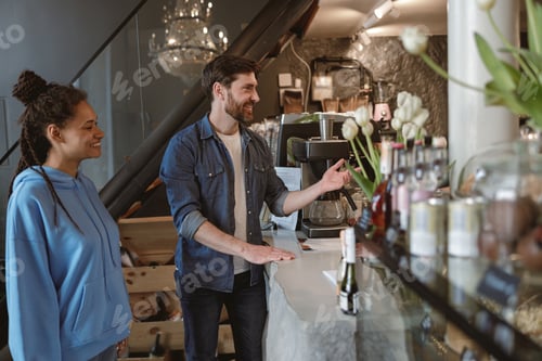 Preview: Mixed-races young couple at cafe ordering drinks and smiling. Luxury cozy place. People on date.