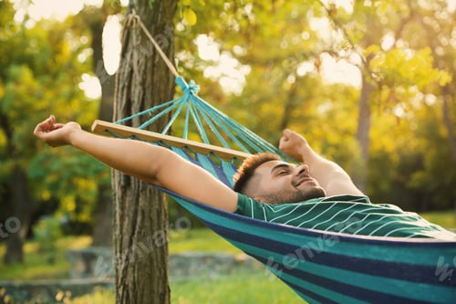 Preview: Young man resting in comfortable hammock at green garden