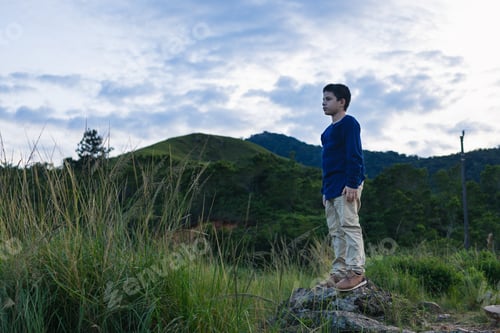 Preview: Hispanic boy standing on the rock looking at the landscape
