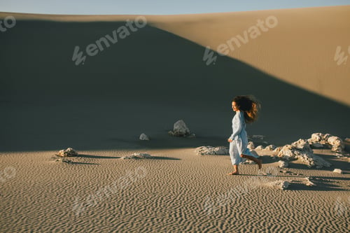 Preview: Woman with long hair in a stylish dress poses in the desert sands.