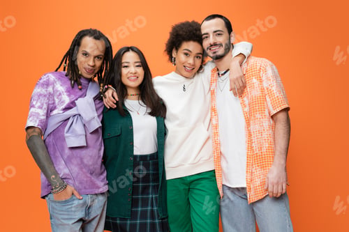 Preview: pleased african american woman hugging trendy multiethnic friends while looking at camera isolated