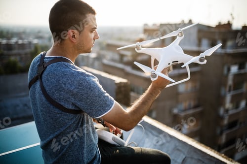 Preview: Young technician flying UAV drone with remote control on rooftop