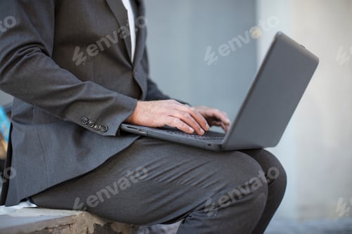 Preview: Businessman working on laptop outside