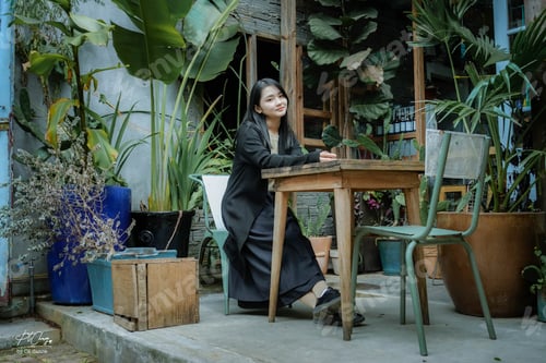 Preview: Woman Sitting at Table Surrounded by Potted Plants