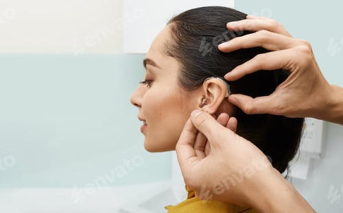 Preview: Installation hearing aid on woman's ear at hearing clinic, close-up, side view. Deafness treatment,