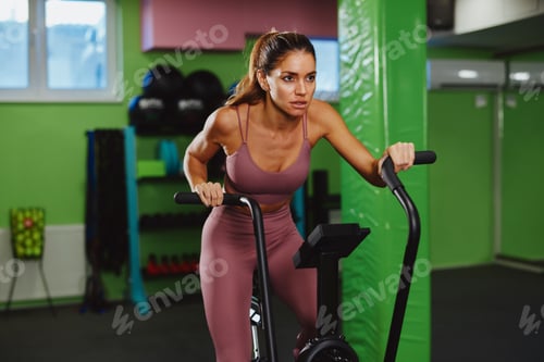 Preview: Determined sportswoman cycling on stationary bike during intense workout session in modern gym