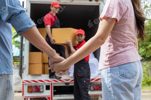 Preview: Young couple checks with two movers unloading boxes and furniture from a pickup truck
