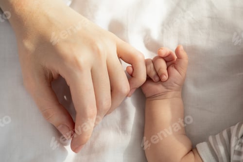 Preview: Mother Baby Connection. Newborn child holding mom's hand while lying in bed
