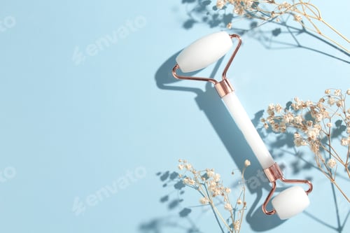 Preview: White jade roller and gua sha tool on pastel blue background. Trendy beauty tool.