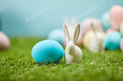 Preview: selective focus of painted easter eggs and toy rabbits on grass with copy space