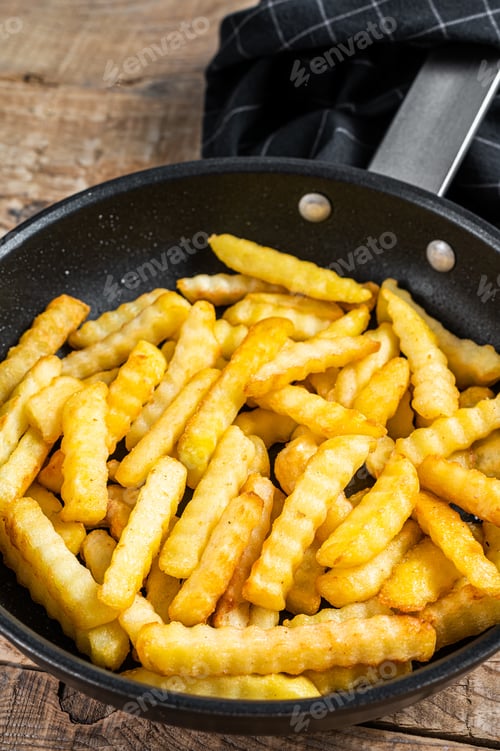 Preview: Deep fried Crinkle French fries potatoes sticks in a pan. Wooden background. Top view