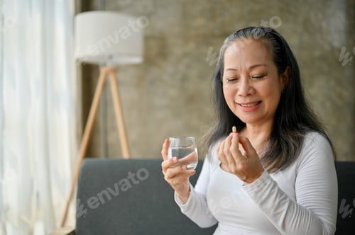 Preview: Wellbeing Asian senior woman drinking water and taking her dietary supplement