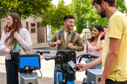 Preview: Joyful Multiethnic Group Renting Electric Bikes on Sunny Day: Asian Guy Arriving with Caucasian Girl
