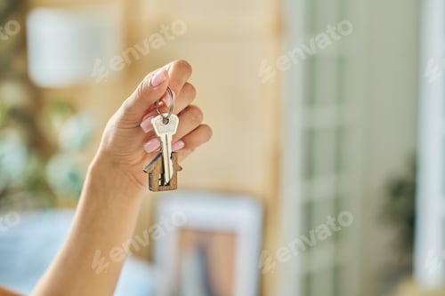 Preview: Hand of young woman holding metallic key with house shaped trinket