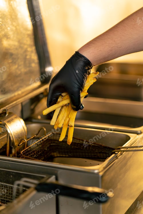 Preview: close-up in a professional kitchen a chef in black gloves puts French fries into a deep fryer