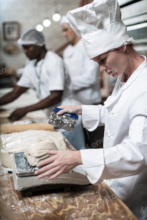 Preview: Female baker weighing dough and cutting it into correct sizes