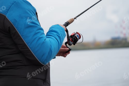 Preview: Fishing. A fishing rod with a reel in the hands of a fisherman. Close-up.
