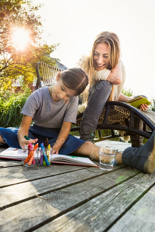 Preview: Daughter sitting on wooden decking drawing with mother