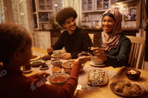 Preview: Happy black Muslim woman eating with her family at dining table.