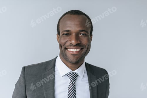 Preview: head and shoulders view of smiling african american businessman looking at camera isolated on grey