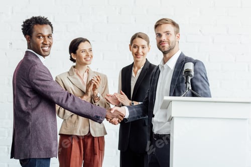 Preview: four multiethnic colleagues in formal wear talking and shaking hands in conference hall