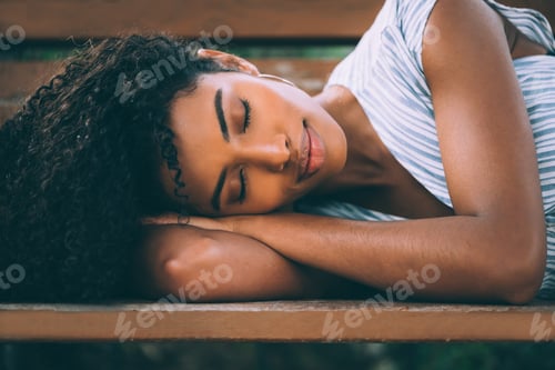 Preview: Beautiful young black woman laying down on a chair in a park