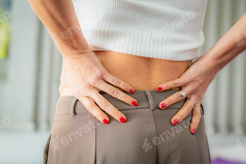Preview: Woman experiencing lower back pain, holding or massaging her sore back with discomfort