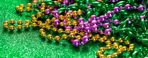 Preview: Mardi Gras concept. Multi-colored beads on green shiny background. Fat Tuesday symbol.