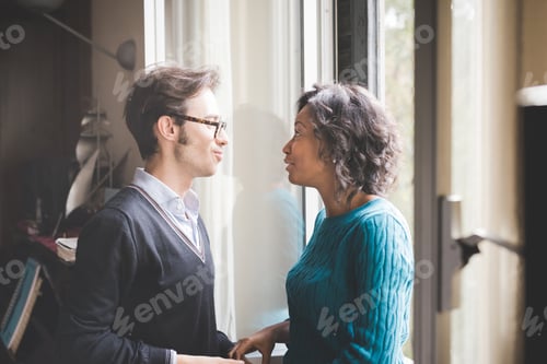 Preview: multiethnic couple of lover having fun and hugging indoor in their house looking eye to eye
