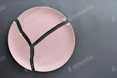 Preview: A broken pink ceramic plate on a gray background. view from above. The concept of diet, old things