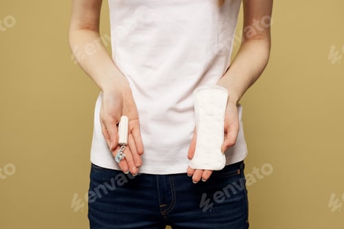 Preview: Girl with a tampon and a pad in her hand on a beige background cropped view of menstruation critical